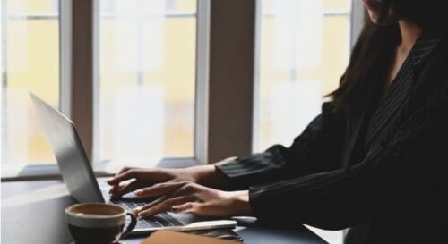 Mujer trabajando en un portátil en una oficina con luz natural, representando el rol esencial de la secretaria de dirección.